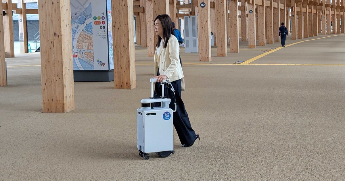 Fotografía oficial de Chieko Asakawa caminando con AI Suitcase bajo la estructura de madera del Gran Anillo de la Expo de Osaka de 2025.
