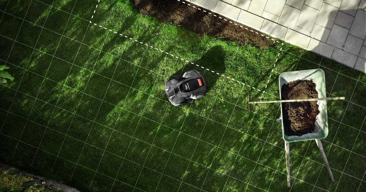 Fotografía oficial cenital de un Automower sobre césped junto a una carretilla y una zona de plantación, con cuadrícula y límites gráficos de AIM superpuestos.