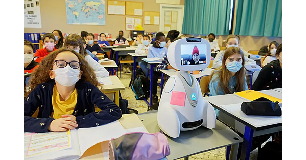 Buddy blanco con pantalla de videollamada junto a alumnos en un aula.