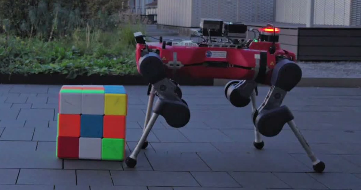 Frame del vídeo oficial de ETH Zúrich: el cuadrúpedo rojo ANYmal junto a un cubo de Rubik gigante en una terraza exterior.