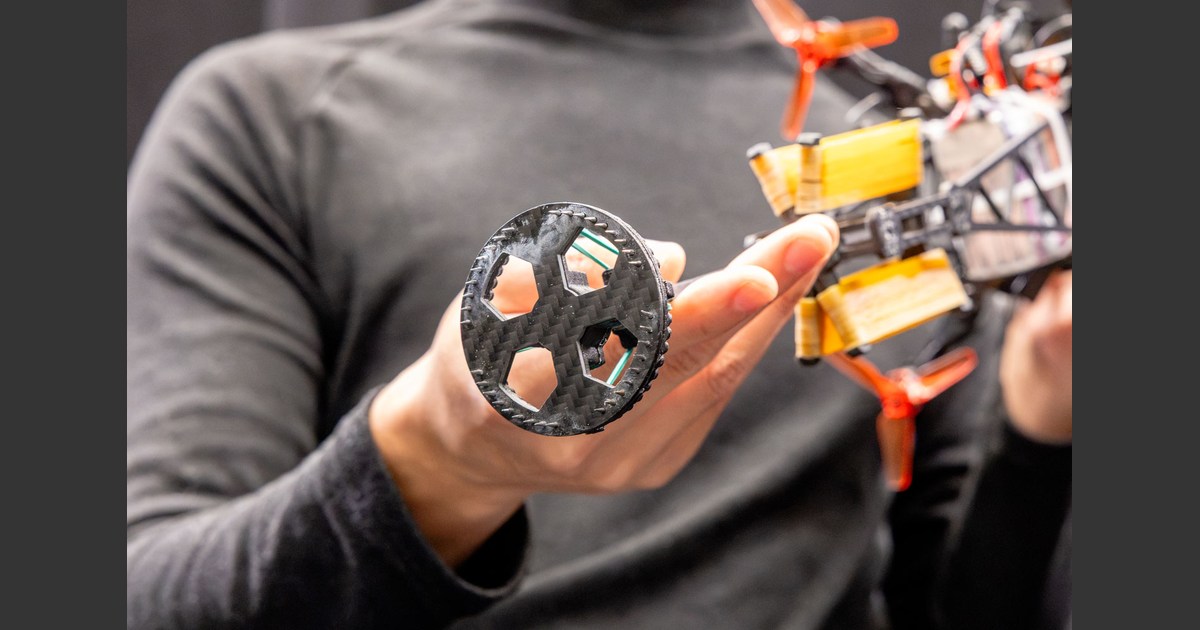 Fotografía de Aaron Demeter: un investigador sostiene Hopcopter y muestra la suela circular con pequeñas púas de su nuevo pie, con las hélices al fondo.
