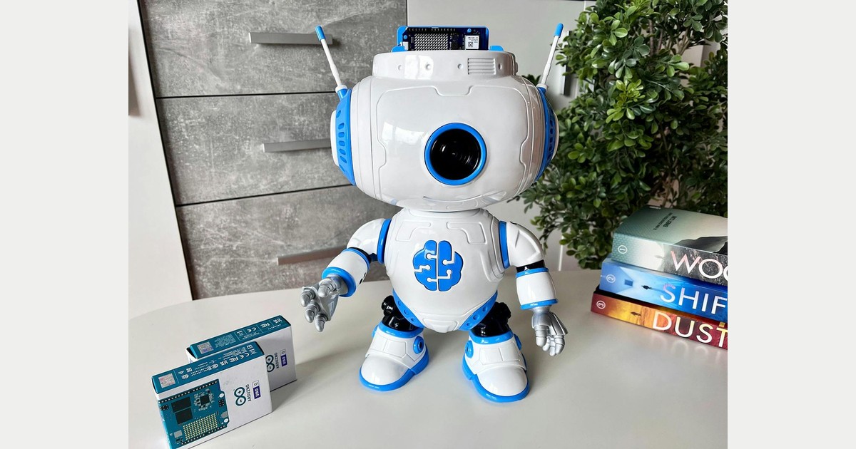 Fotografía del creador de JBR-001 con el robot blanco y azul sobre una mesa, cámara frontal y placa Arduino UNO Q visible encima de la cabeza.