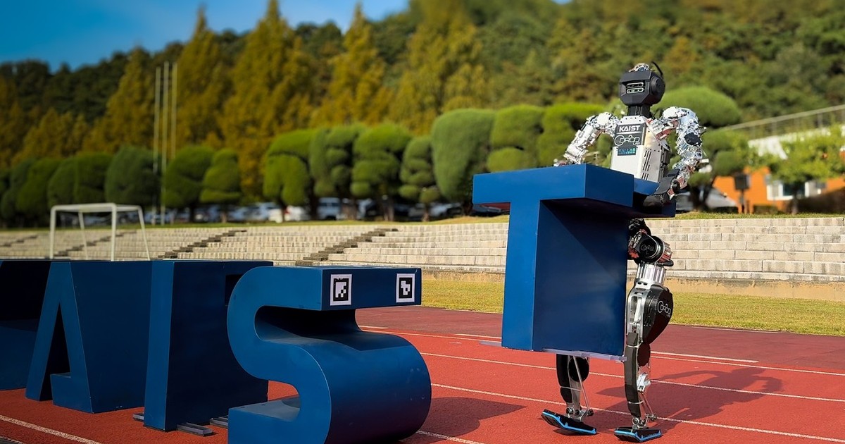 El humanoide de KAIST sostiene una gran letra T azul sobre una pista de atletismo, junto a otras letras de la demostración.