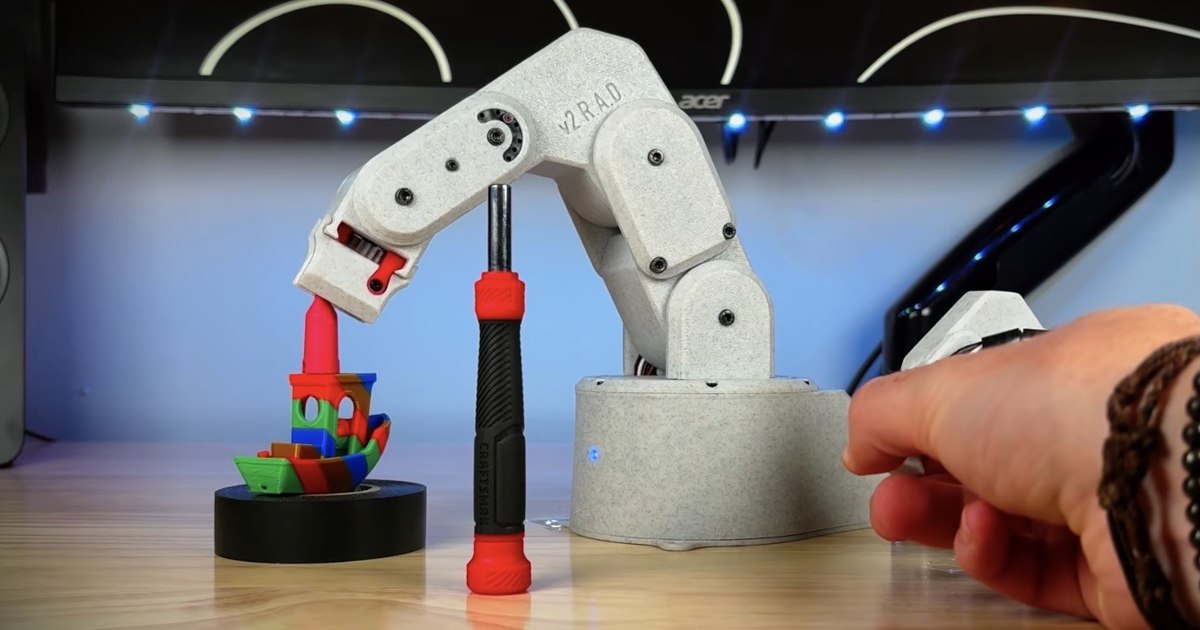 Fotografía del brazo robótico R.A.D. v2 impreso en 3D, con su pinza junto a una pieza de colores sobre una mesa.