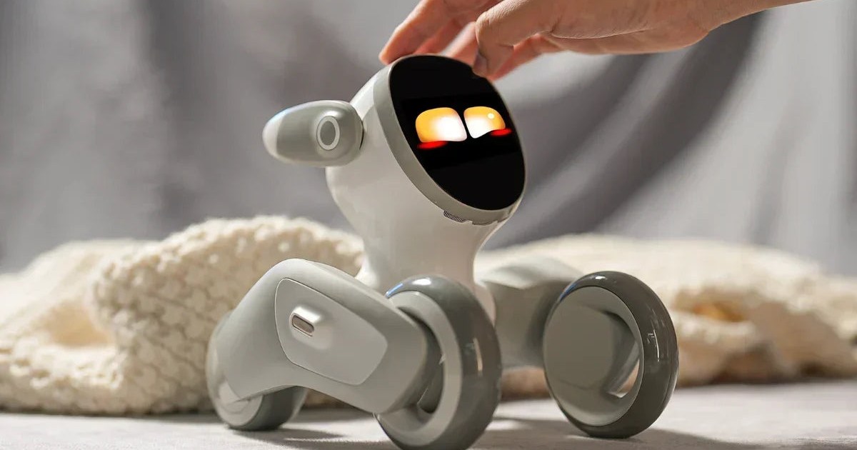 Fotografía oficial de una mano acariciando la cabeza de Loona Petbot, con los ojos amarillos iluminados y las ruedas apoyadas en una superficie clara.