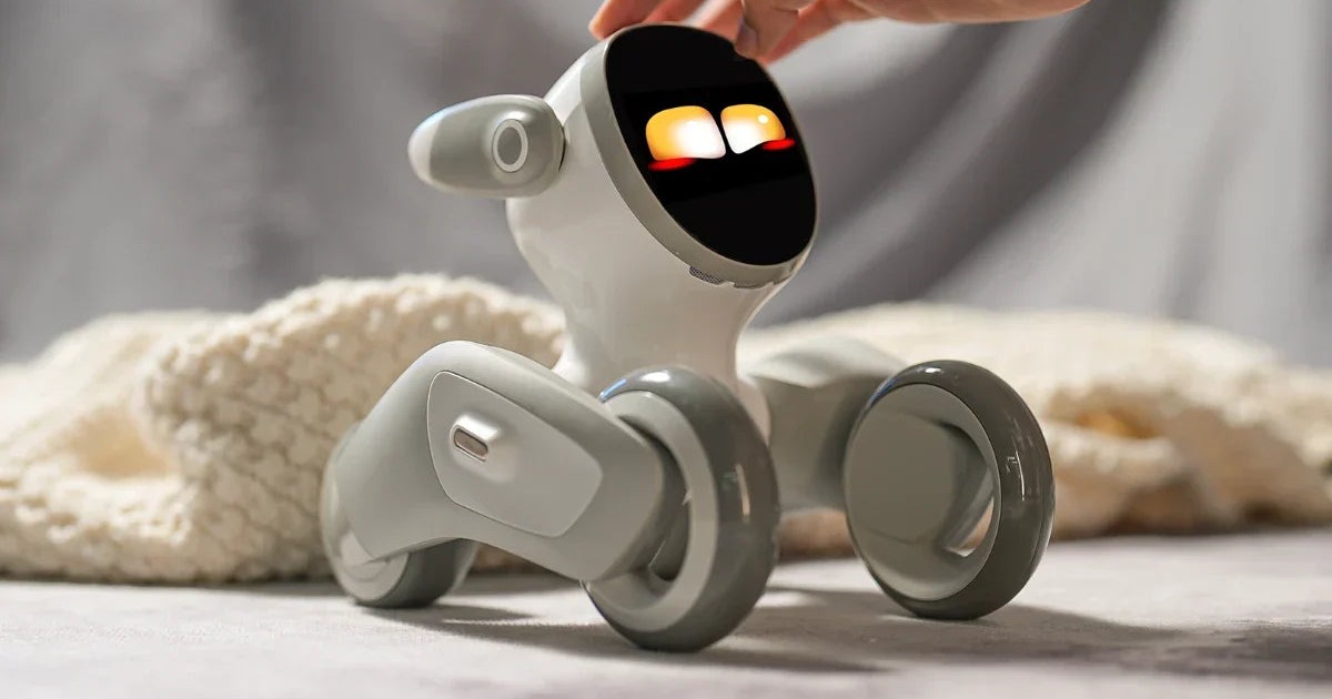Una mano acaricia la cabeza de Loona Petbot, con los ojos iluminados y las cuatro ruedas apoyadas sobre una superficie junto a una manta, en una fotografía oficial.