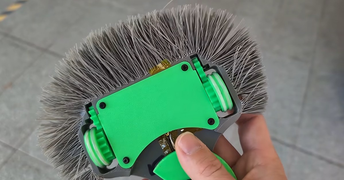 Fotograma de Maker's Muse: una mano sostiene boca abajo un pequeño robot de combate verde y gris, rodeado de largas cerdas de plástico.