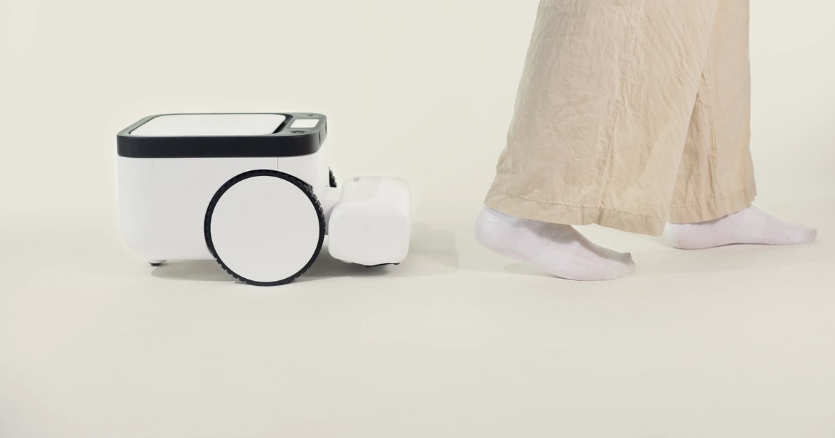Fotografía promocional oficial de un robot Matic blanco de perfil junto a los pies de una persona con pantalones claros.