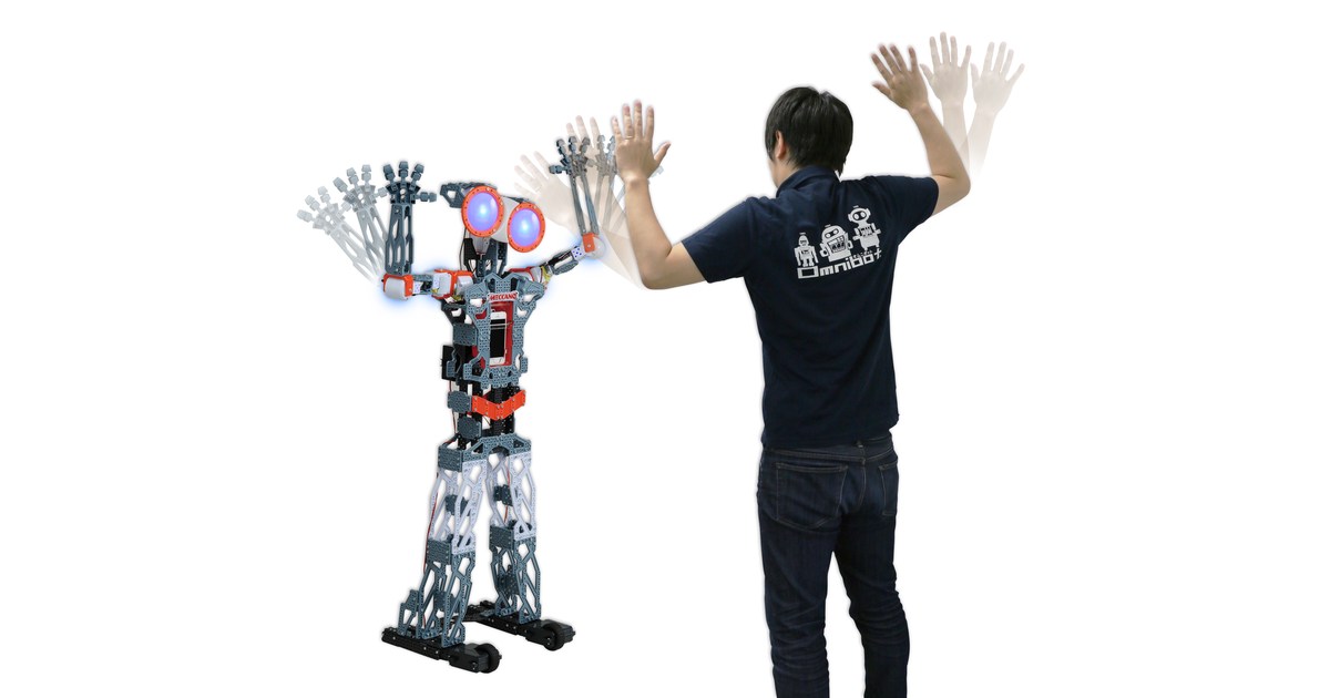 Meccanoid G15KS completo junto a una persona que realiza un gesto con los brazos, en una fotografía promocional de Takara Tomy.
