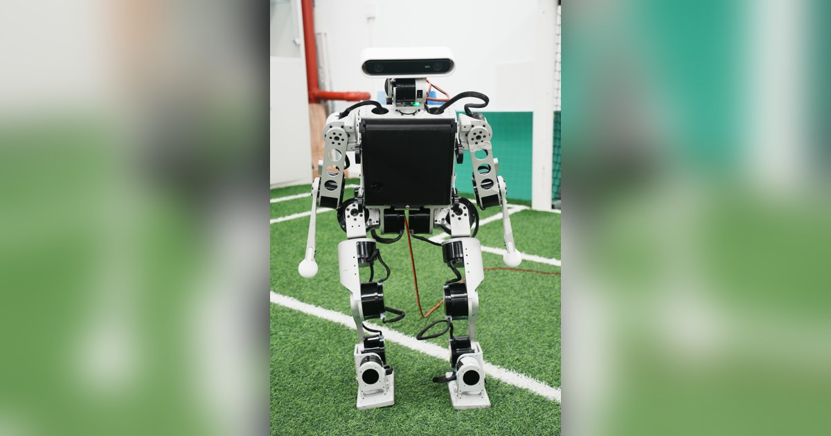 Fotografía oficial de MOS9.2 completo, de frente, con estructura metálica, brazos y pies sobre un campo de fútbol robótico.