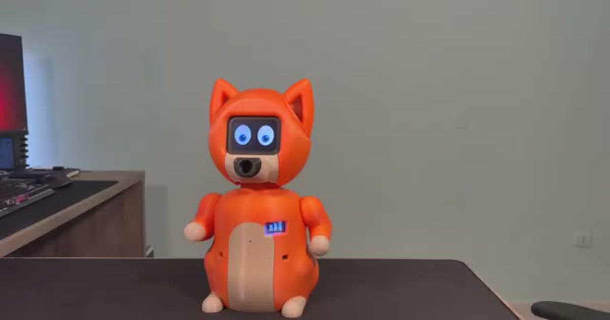 Fotograma del vídeo de Luca Di Lorenzo para Arduino: el robot Nuvi naranja, con ojos animados, orejas y brazos, sobre una mesa.