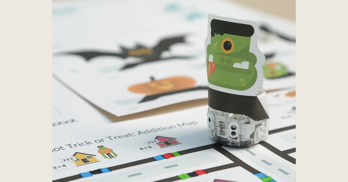 Fotografía oficial de Ozobot Evo con un disfraz de papel verde sobre el mapa de Halloween, entre líneas de colores y casas con operaciones.