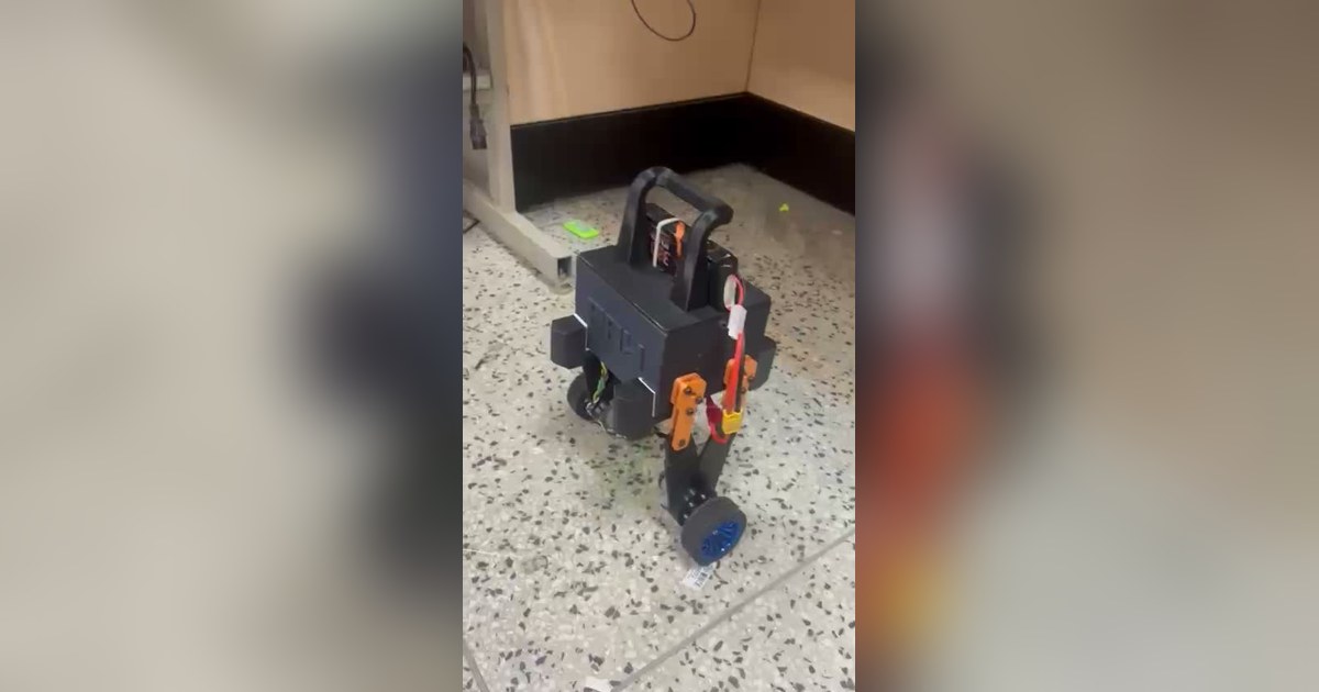 Fotograma del vídeo de Sndcooper con PAW completo, cuerpo negro, patas articuladas naranjas y dos ruedas, en un ensayo sobre el suelo.