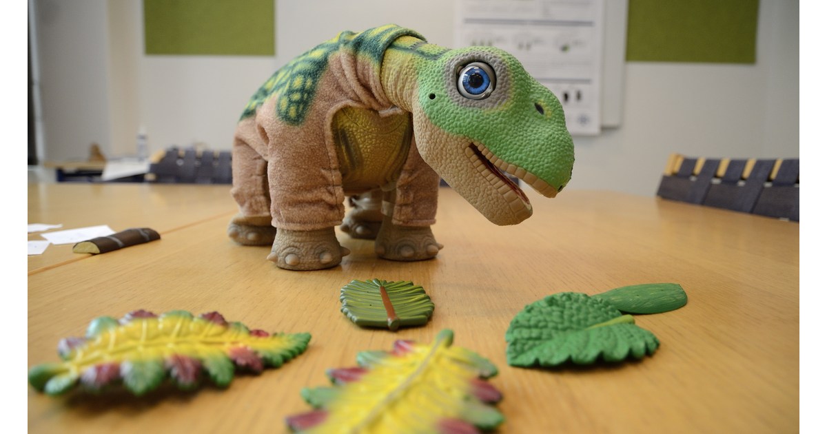 PLEO rb sobre una mesa del laboratorio de interacción humano-robot de la SDU, junto a sus hojas de juego.