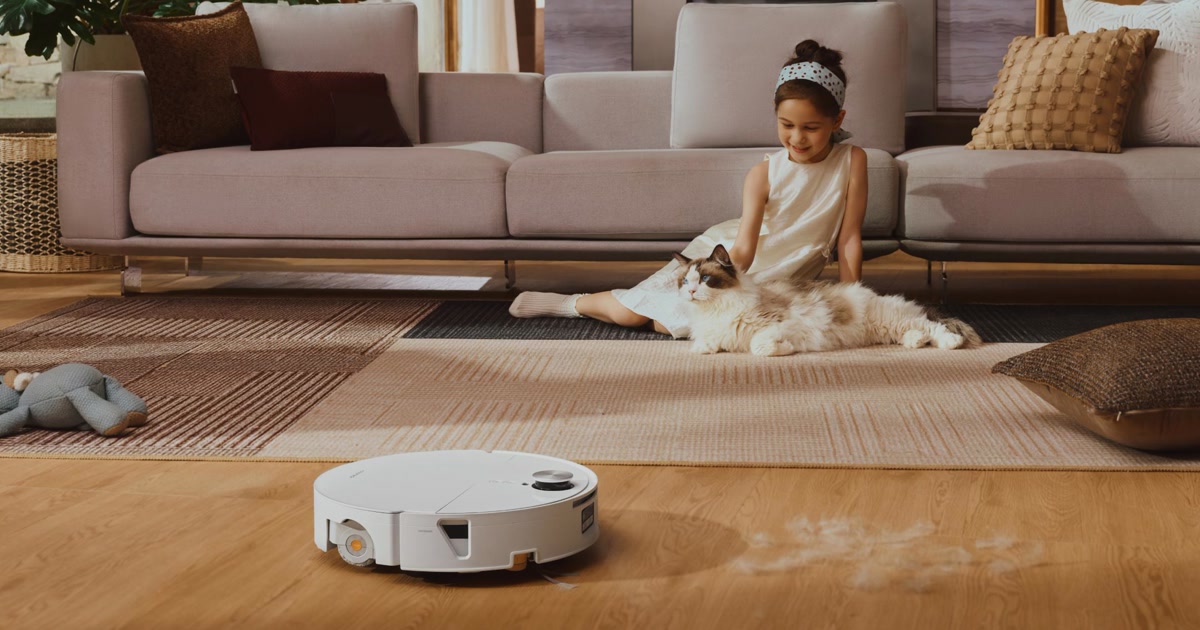 Fotografía promocional oficial del Roborock Saros 20 Flow blanco sobre suelo de madera, junto a una alfombra con una niña y un gato.