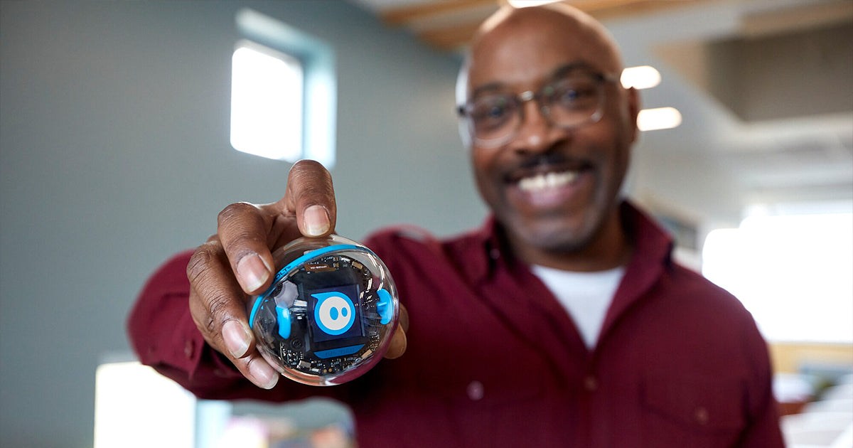 Fotografía oficial de un hombre sosteniendo un Sphero BOLT+ transparente, con una cara azul en su pantalla y el robot enfocado en primer plano.