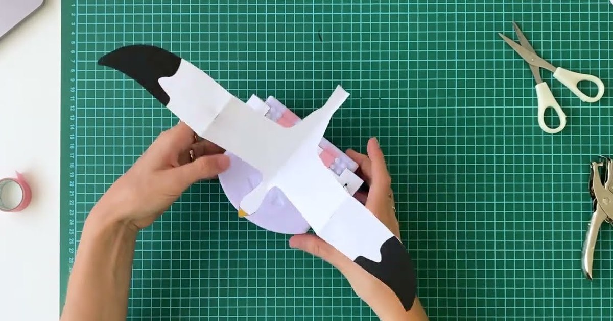 Imagen del tutorial oficial de EPFL: unas manos sostienen un Thymio con un ave de papel acoplada, sobre una base de corte verde.