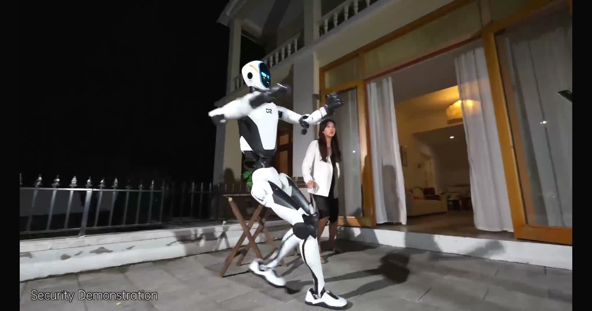Frame del vídeo oficial de Unitree: H2-X se coloca delante de una mujer en una escena preparada de protección junto a una vivienda.