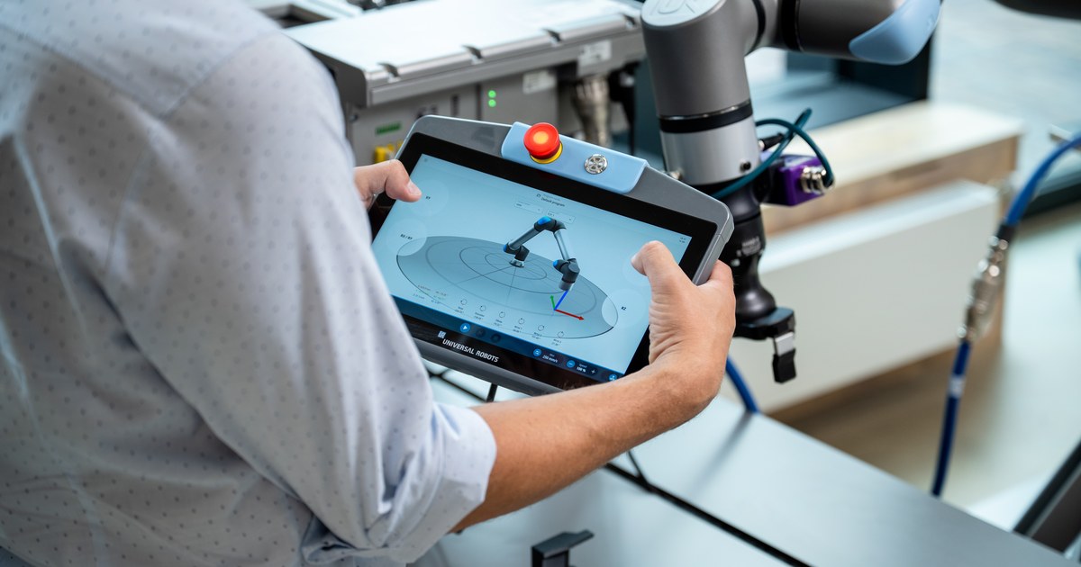 Una persona maneja la consola de programación junto a un brazo de Universal Robots, en una fotografía oficial de la plataforma Gen 7.