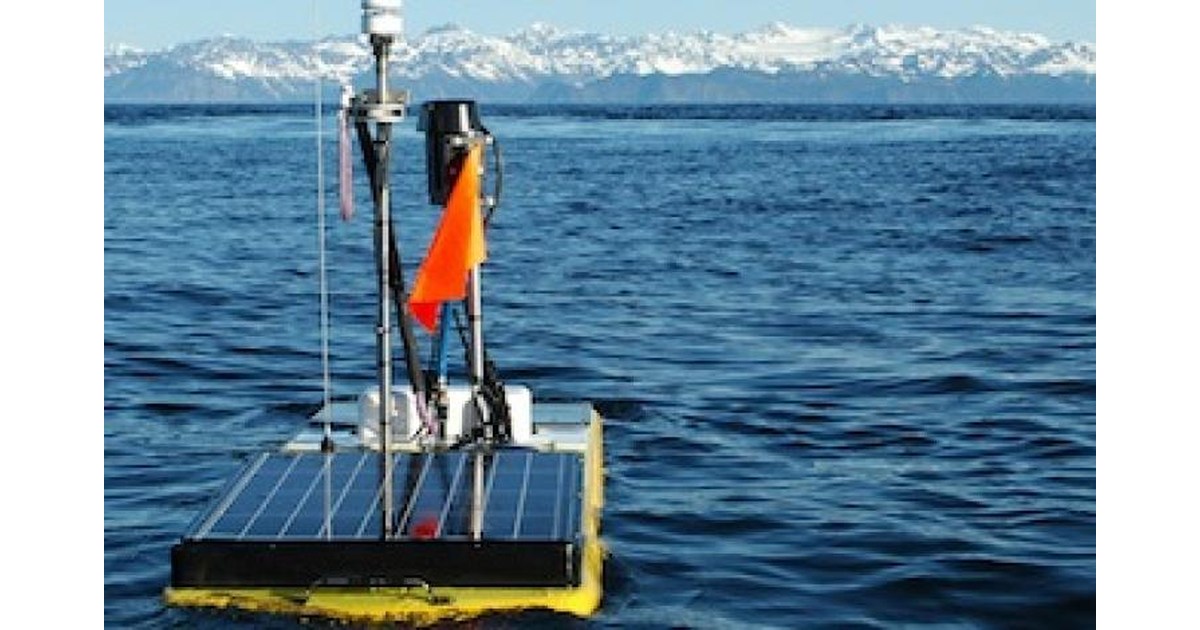 Wave Glider con paneles solares y mástil navegando en Prince William Sound, con montañas al fondo.
