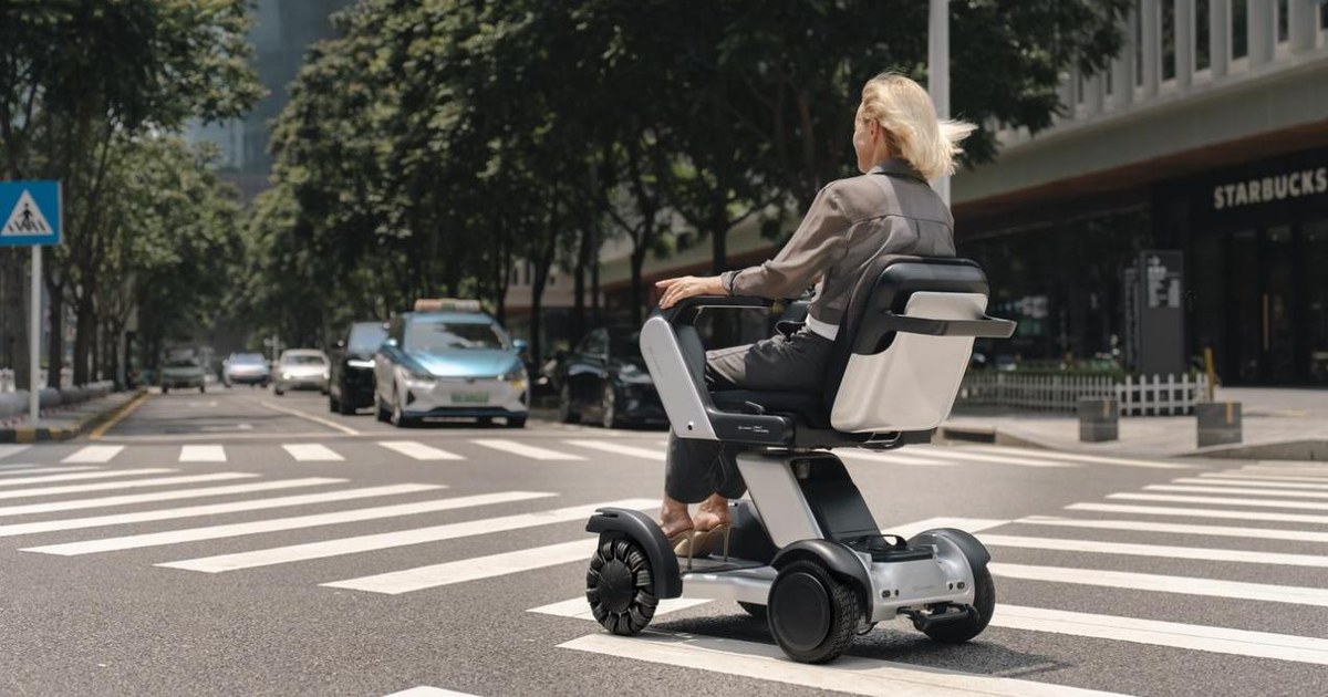 Una persona sentada en el Xcanbot Mate X junto a un paso de peatones, vista desde atrás, en una fotografía oficial de la empresa.