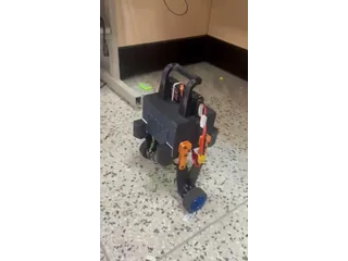 Fotograma del vídeo de Sndcooper con PAW completo, cuerpo negro, patas articuladas naranjas y dos ruedas, en un ensayo sobre el suelo.