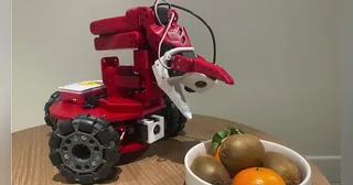 LeKiwi rojo con brazo, cámaras y base móvil de tres ruedas omnidireccionales.