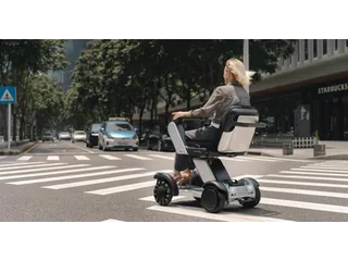 Una persona sentada en el Xcanbot Mate X junto a un paso de peatones, vista desde atrás, en una fotografía oficial de la empresa.