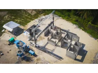 Vista aérea de una impresora COBOD BOD3 trabajando sobre los muros de un edificio en Indonesia, junto a su sistema de suministro de material.
