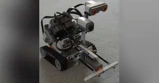 Construcción LEGO NXT 2.0 sobre orugas con sensores y mecanismo frontal visibles.