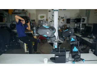 Blue en una demostración de teleoperación con sus dos brazos y un operador al fondo.