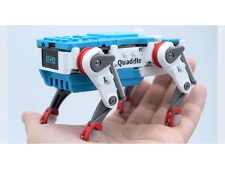 Fotografía de un Petoi Quaddle azul y blanco sobre la palma de una mano, con los mecanismos de sus patas visibles; miniatura del vídeo oficial.