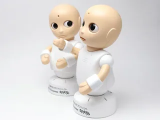 Dos robots CommU blancos de sobremesa con ojos y cabeza articulados.