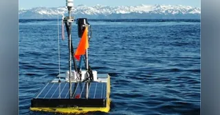 Wave Glider con paneles solares y mástil navegando en Prince William Sound, con montañas al fondo.