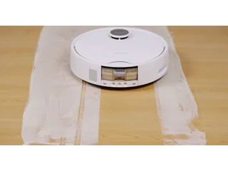 SwitchBot S20 blanco fregando una franja de suciedad sobre madera, fotograma de una demostración oficial del fabricante.