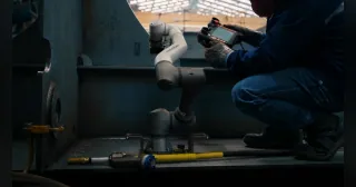 Robot de soldadura ArcLift GO de HD Hyundai trabajando junto a un operario dentro de una estructura de acero en un astillero.
