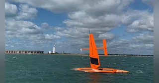 Saildrone Explorer naranja identificado como SD 1021 navegando por el mar con su vela rígida.