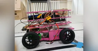 Fotografía de KU STEAM Pinkies de su coche robot completo visto de lado, con chasis rosa por niveles, cuatro ruedas y cableado visible.