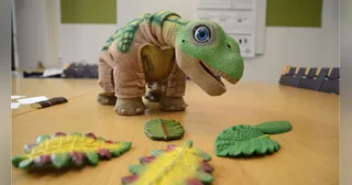PLEO rb sobre una mesa del laboratorio de interacción humano-robot de la SDU, junto a sus hojas de juego.