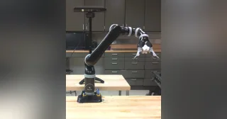 Fotografía completa del brazo Kinova MICO de seis ejes y pinza de dos dedos, fijado con su base a una mesa de laboratorio.