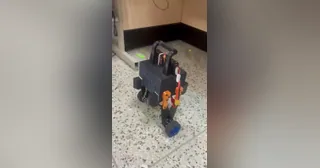 Fotograma del vídeo de Sndcooper con PAW completo, cuerpo negro, patas articuladas naranjas y dos ruedas, en un ensayo sobre el suelo.