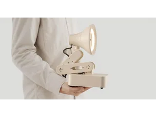 Fotografía oficial de Autonomous Lamp de color arena, con el aro luminoso encendido, sostenido por una persona con jersey claro.