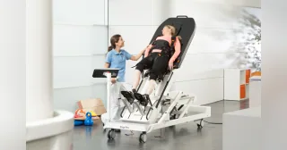 ErigoPro con un paciente sujeto a la mesa inclinada y una profesional junto al mando.