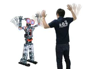Meccanoid G15KS completo junto a una persona que realiza un gesto con los brazos, en una fotografía promocional de Takara Tomy.