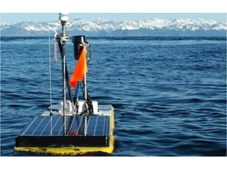 Wave Glider con paneles solares y mástil navegando en Prince William Sound, con montañas al fondo.