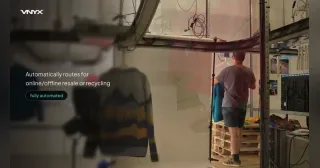 Fotograma de la línea VNYX100 en funcionamiento, con una prenda suspendida en el transportador y un operario al fondo.
