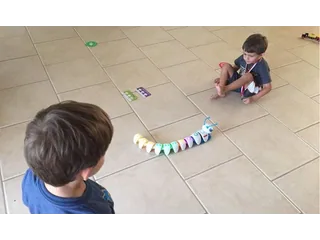 Code-a-pillar completo con varios segmentos conectados sobre un suelo de baldosas durante una actividad con niños.