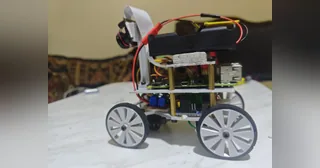 Fotografía de The Red Castle de su coche robot completo visto de lado, con cuatro ruedas grises, cámara elevada y chasis de varios niveles.