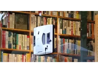 HOBOT-S7 Pro conectado por cable y adherido a un cristal frente a una estantería.