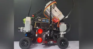 Fotografía del Team Terminator de su coche robot completo visto de lado, con chasis LEGO, ruedas negras, sensores y luces rojas.
